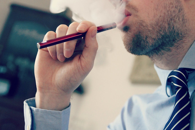 man in a shirt and a tie vaping a red disposable vape pen