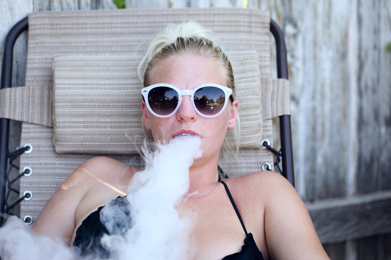 girl vaping on a sun bed wearing sunglasses