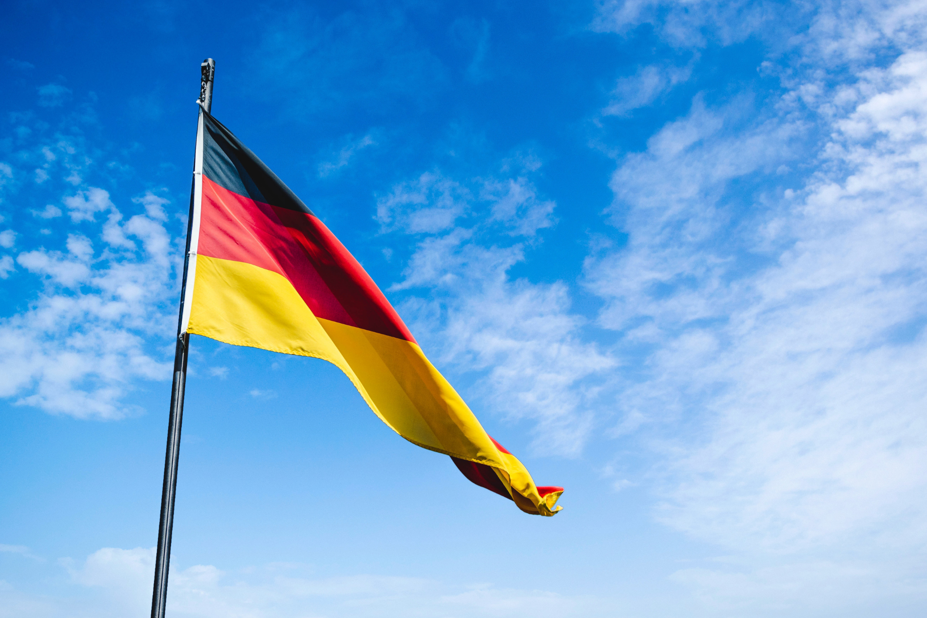 A German flag flying in a blue sky with white cloud
