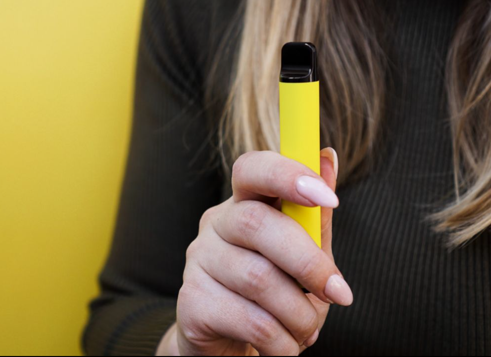 lady with pink nails holds a yellow pen-shaped disposable vape device