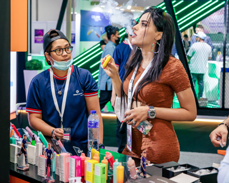 geekvape stand representative helping a customer try out new geekvape vape disposables at the world vape show dubai 2022 - brown haired female vaping geekvape products