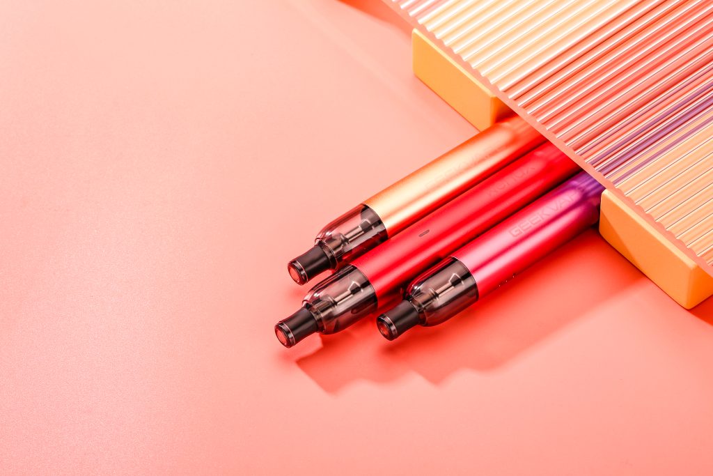 three wenax m1 vape devices in pink, red and yellow casings in a promotional shot for geekvape